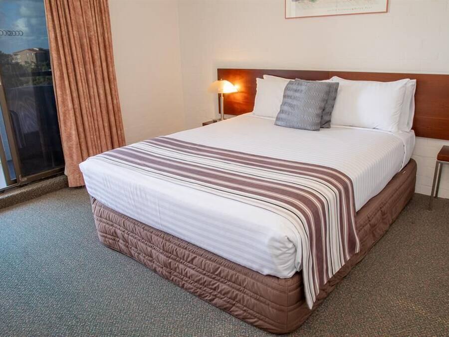 Una habitación de hotel con una cama grande, una mesita de noche, una lámpara y una ventana con cortinas.