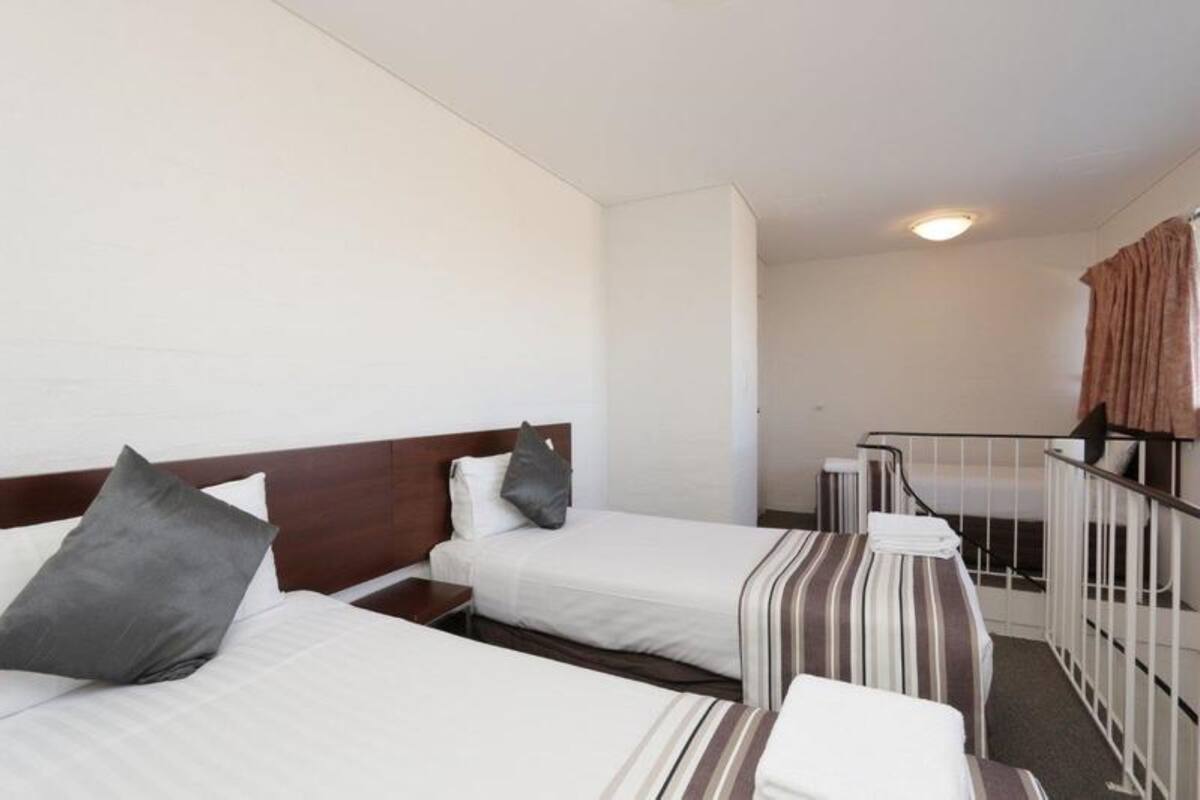 A hotel room with two beds, a small desk, and a staircase leading to an upper level.