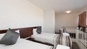 A hotel room with two beds, a small desk, and a staircase leading to an upper level.