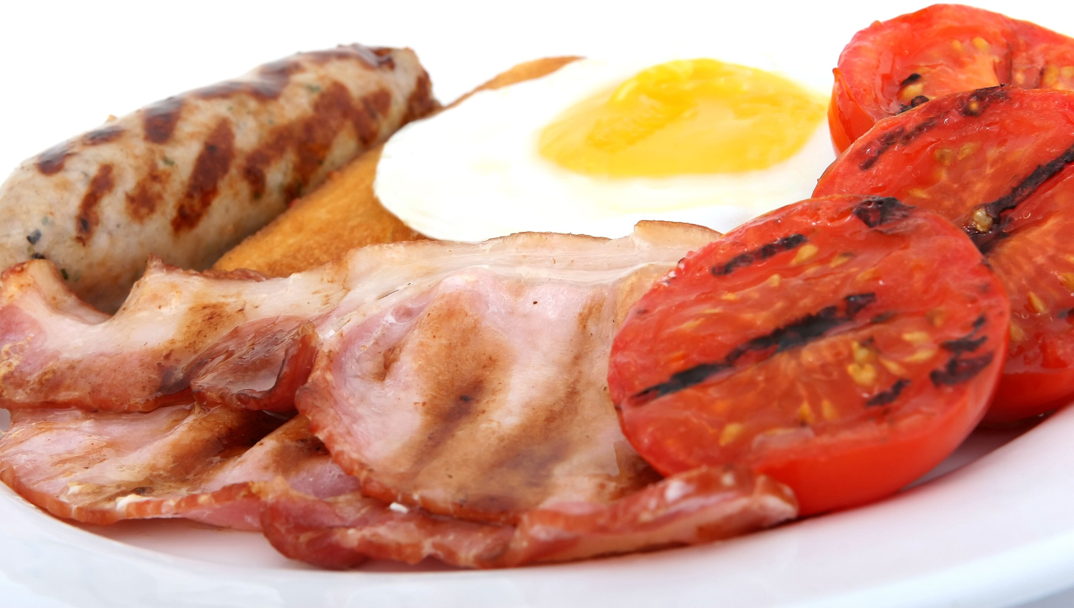 Un piatto di cibo con salsicce grigliate, pancetta, un uovo fritto e fette di pomodoro alla griglia.