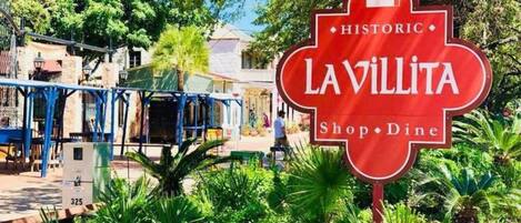 A red sign with 'LAVILLITA Shop · Dine' and 'HISTORIC' written on it, surrounded by greenery and a building in the background.