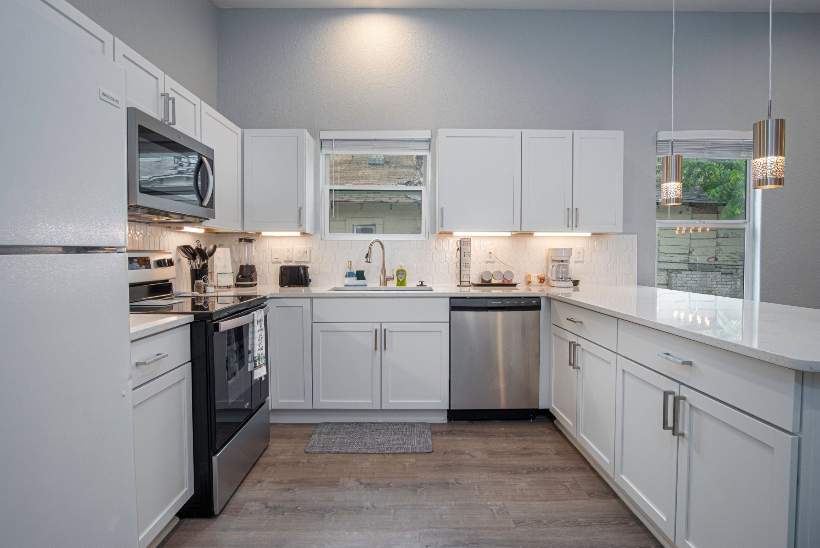 A modern kitchen with white cabinets, stainless steel appliances, and a wooden floor.