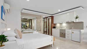 A modern bedroom with a large bed, a built-in desk, and a kitchenette. - Luxe King Studio in Santai (Tweed)