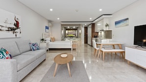 A modern living room with a sofa, coffee table, and dining area. - Luxe King Studio in Santai (Tweed)