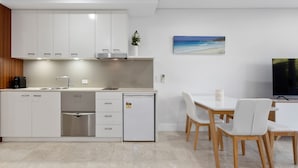 A modern kitchen with white cabinets, a built-in oven, and a dining area with a table and chairs. - Luxe King Studio in Santai (Tweed)