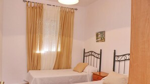 A bedroom with two single beds, a wooden nightstand, a small table, and a window with curtains. - Cervantes Apartment in Conil (Conil de la Fra)