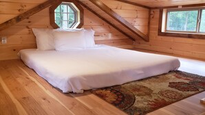 Dormitorio de cabaña de madera con una cama, una ventana y piso de madera.