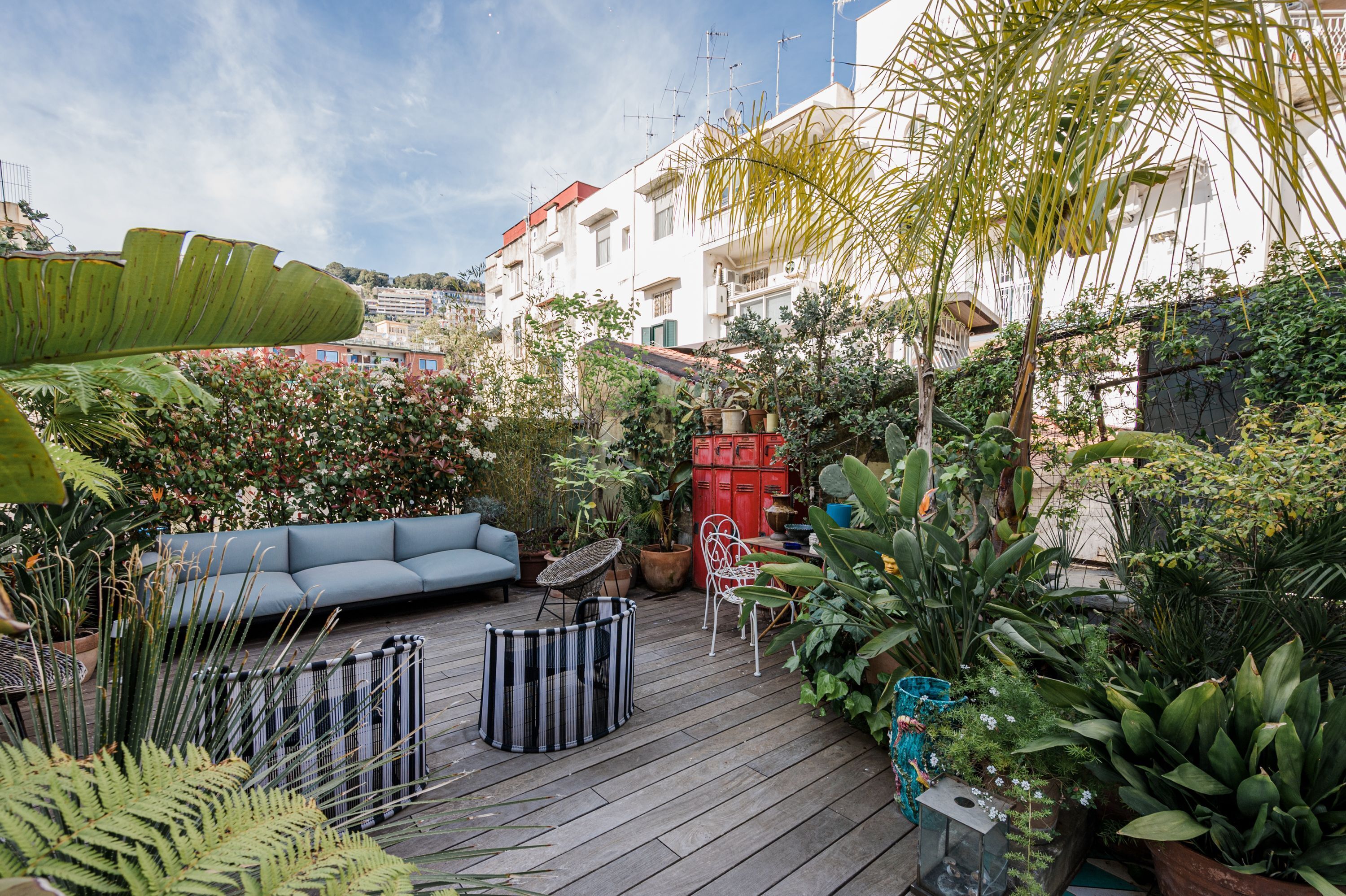 A wooden deck with a blue sofa, metal chairs, and potted plants.