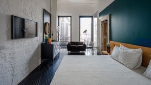 Habitación de hotel moderna con una cama grande, un sofá de color oscuro, una mesita y vistas de la ciudad a través de amplias ventanas.