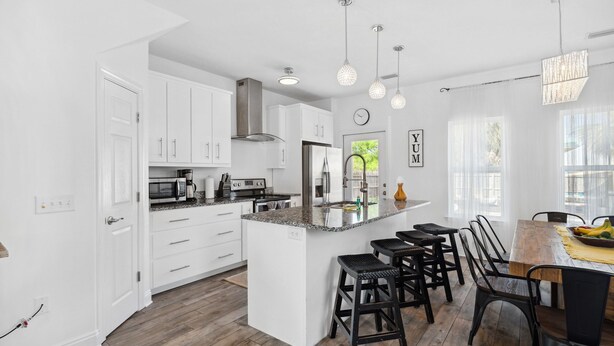 A modern kitchen with white cabinets, a central island with bar stools, and pendant lighting. - Family Getaway•4BR•Games•Fire Pit•Easy Beach Access•Fenced Yard•Pet Friendly  (Panama City Beach)