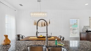 A modern kitchen with granite countertops, a stainless steel sink, a wooden dining table, and a pendant light. - Family Getaway•4BR•Games•Fire Pit•Easy Beach Access•Fenced Yard•Pet Friendly  (Panama City Beach)