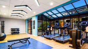 Une salle de sport équipée de tapis de course, d’un banc et de ballons d’exercice.