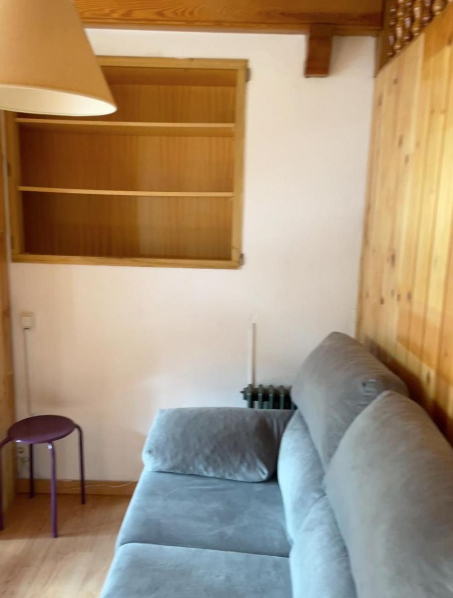 A room with a grey sofa, a wooden shelf unit, and a small purple stool.
