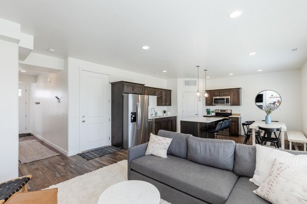 A modern living room with a gray sofa, a round coffee table, and a dining area with a white table and chairs.