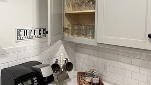 Une cuisine équipée d’un coin café, comprenant une machine à café, des tasses et un panneau indiquant : « CAFÉ FRAÎCHEMENT PREPARÉ TOUTE LA JOURNÉE ».