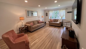 Un salon spacieux comprenant un canapé, un fauteuil et un téléviseur à écran plat fixé au mur.