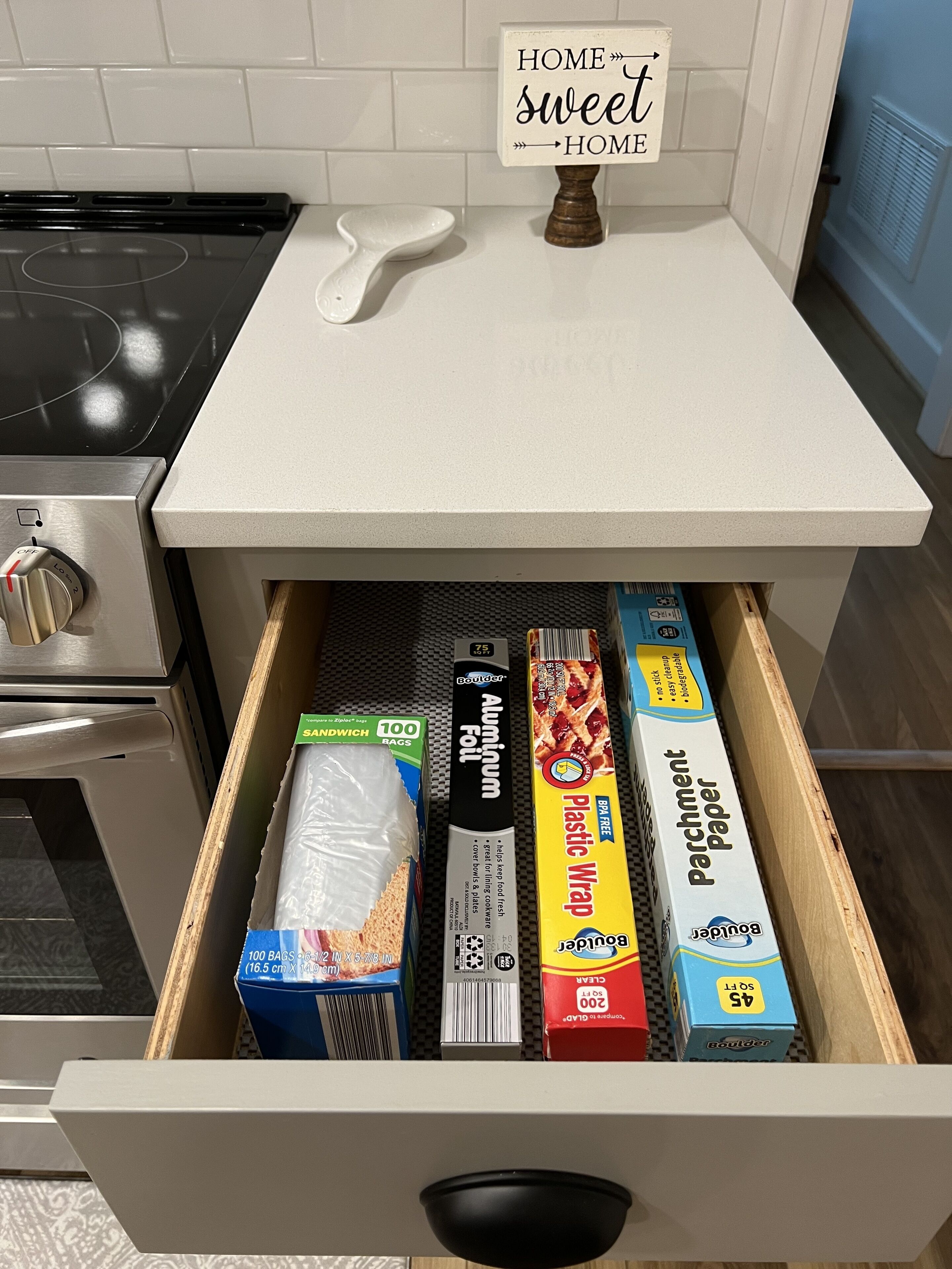 A kitchen drawer with various food items including aluminum foil, plastic wrap, parchment paper, and sandwich bags.
