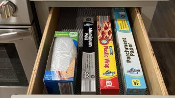 A kitchen drawer with various food items including aluminum foil, plastic wrap, parchment paper, and sandwich bags.
