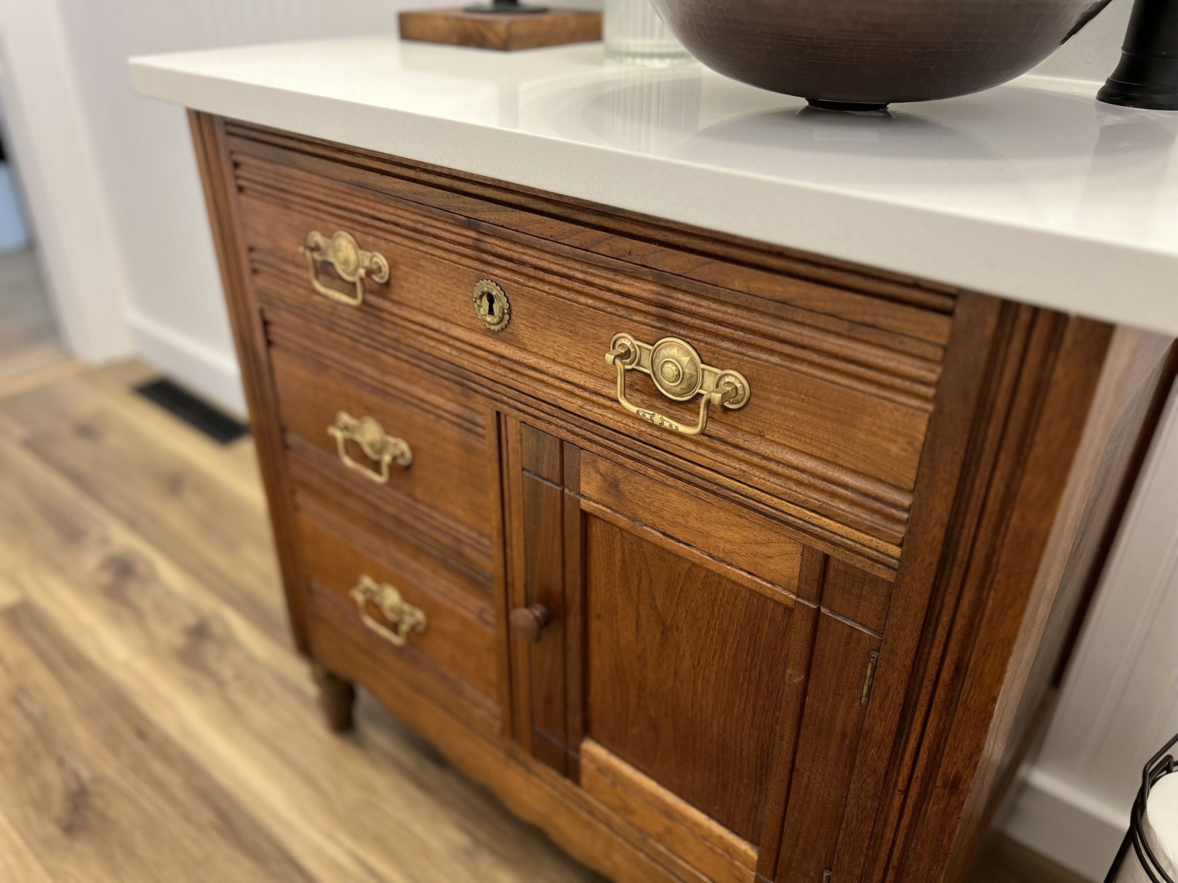 A wooden dresser with brass handles and a white countertop.