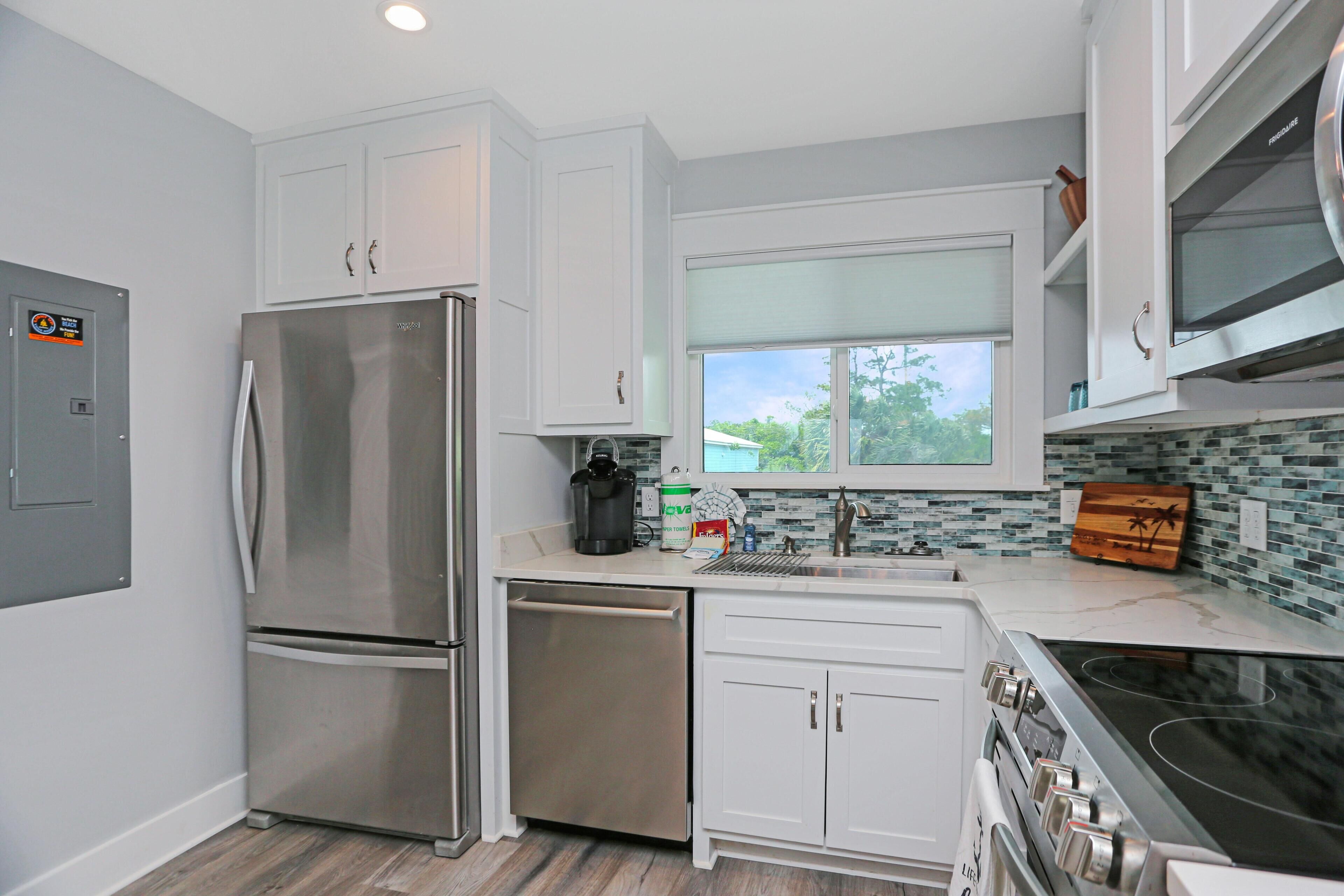 A modern kitchen with stainless steel appliances, white cabinetry, and a large window providing natural light.