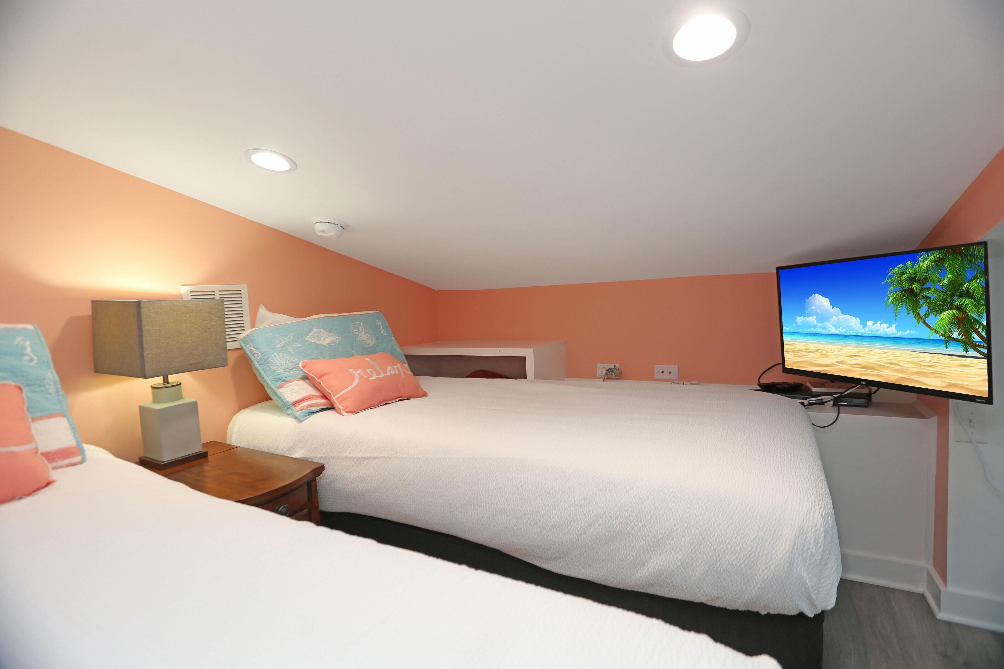 A hotel room with two beds, a TV, and a ceiling light.