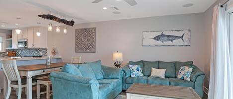 Een moderne woonkamer met een turquoise bank, een houten salontafel, en een eethoek met een witte tafel en stoelen.