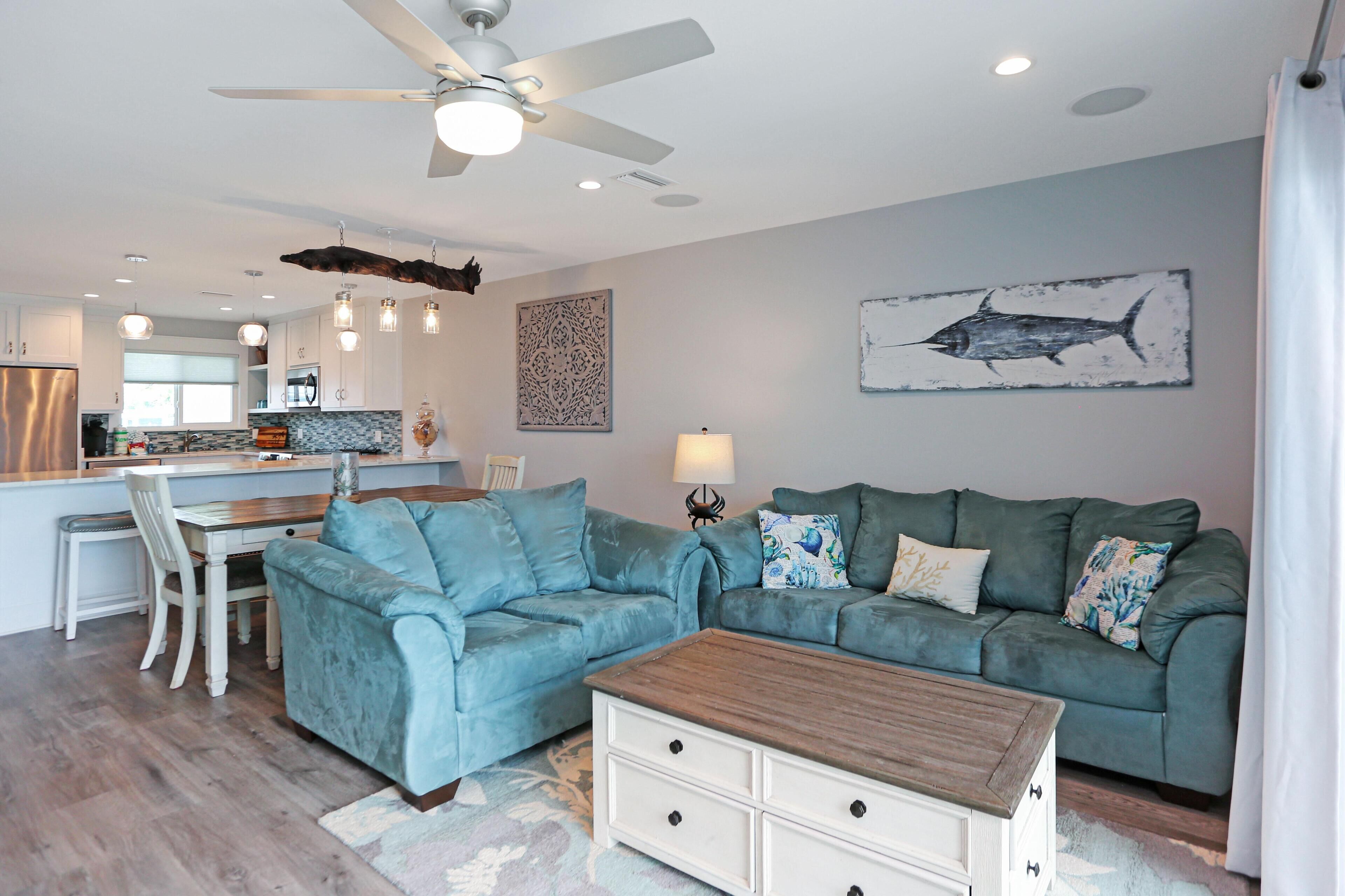 A modern living room with a teal sofa, a wooden coffee table, and a ceiling fan.