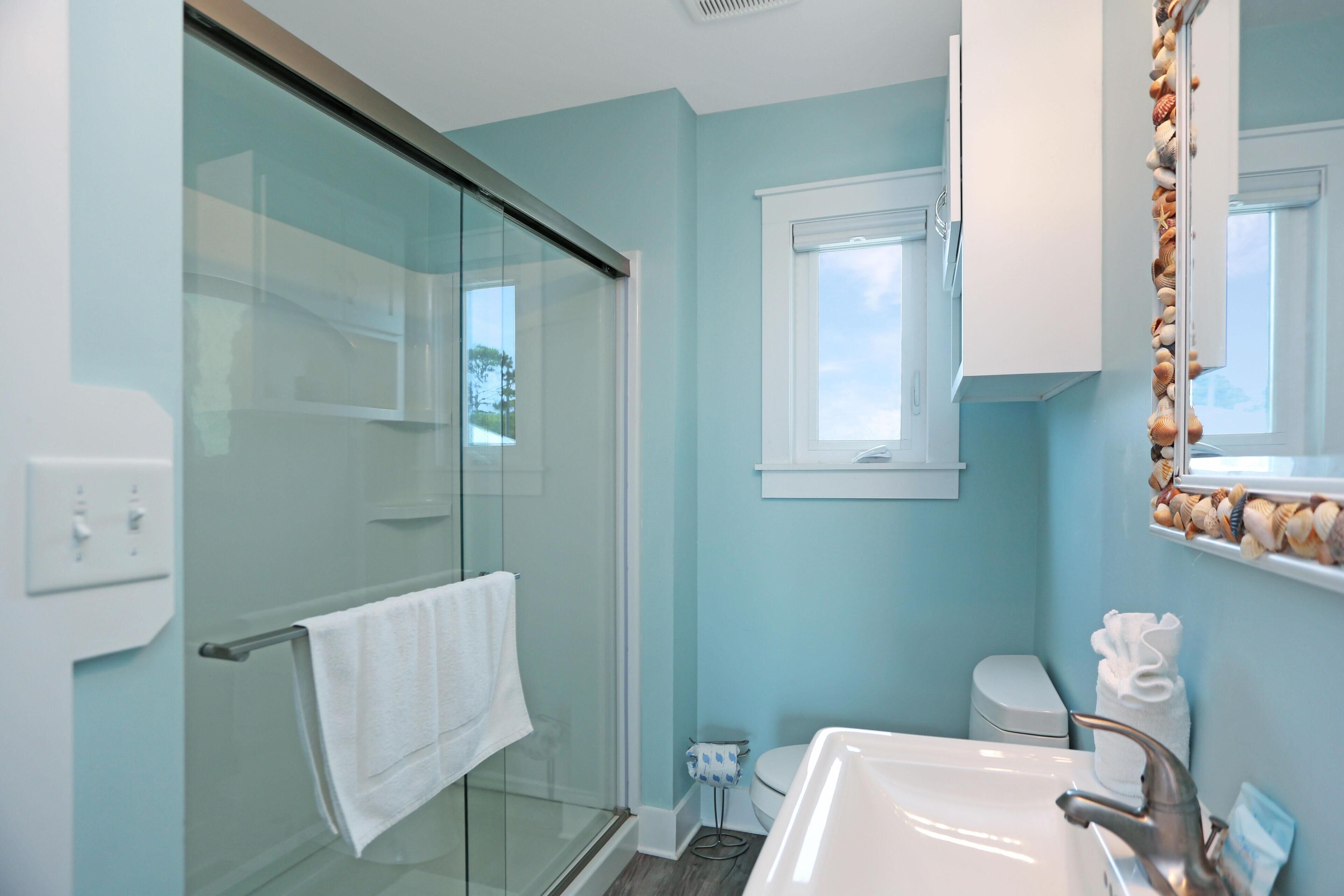 A bathroom with a glass shower enclosure, a white sink, and a toilet.
