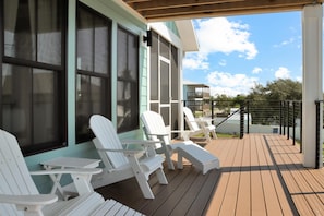 Une terrasse extérieure couverte, dotée de chaises Adirondack blanches et d’une table, qui offre une vue sur un quartier résidentiel.
