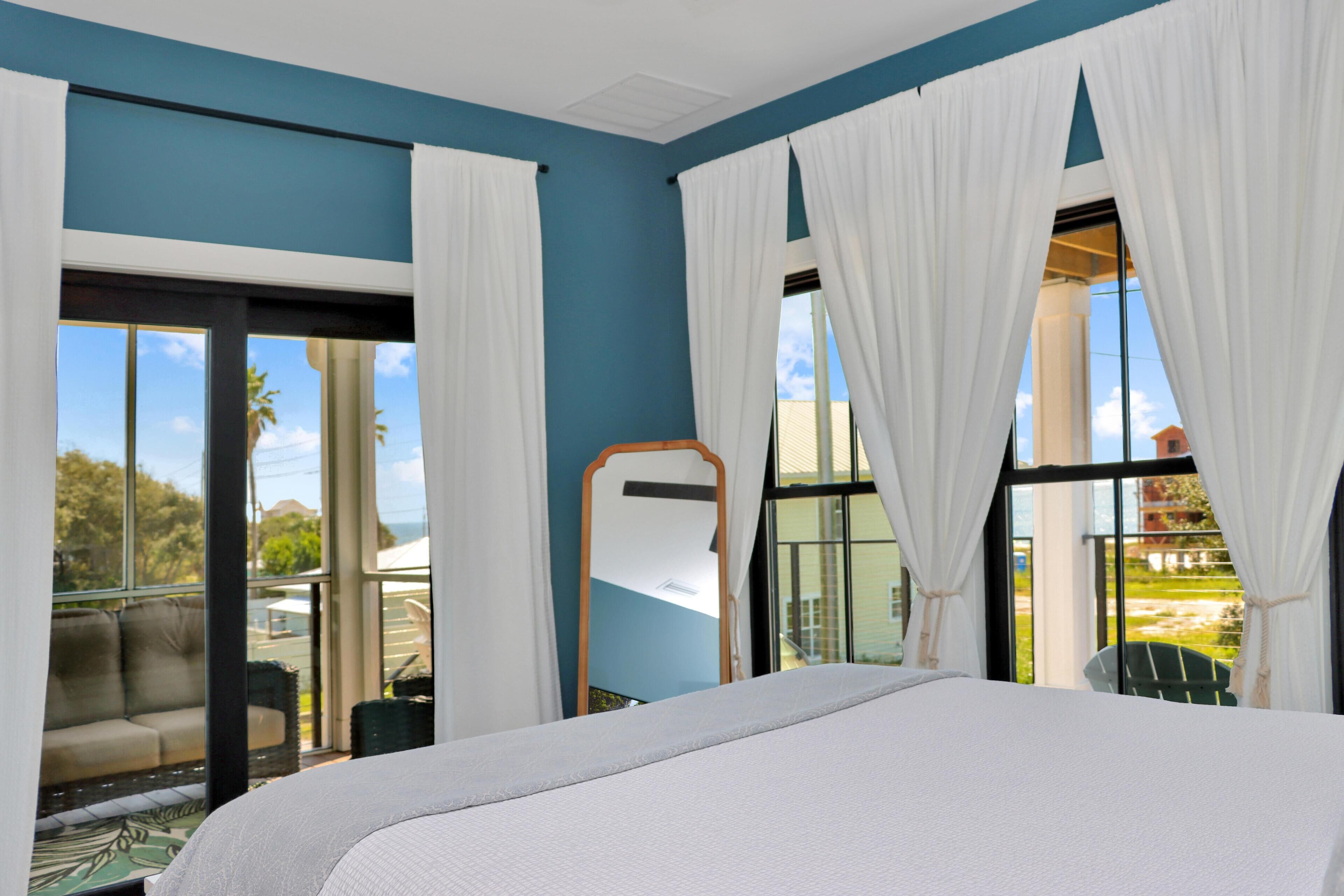 Een hotelkamer met een groot bed, een balkon met uitzicht en een raam met witte gordijnen.