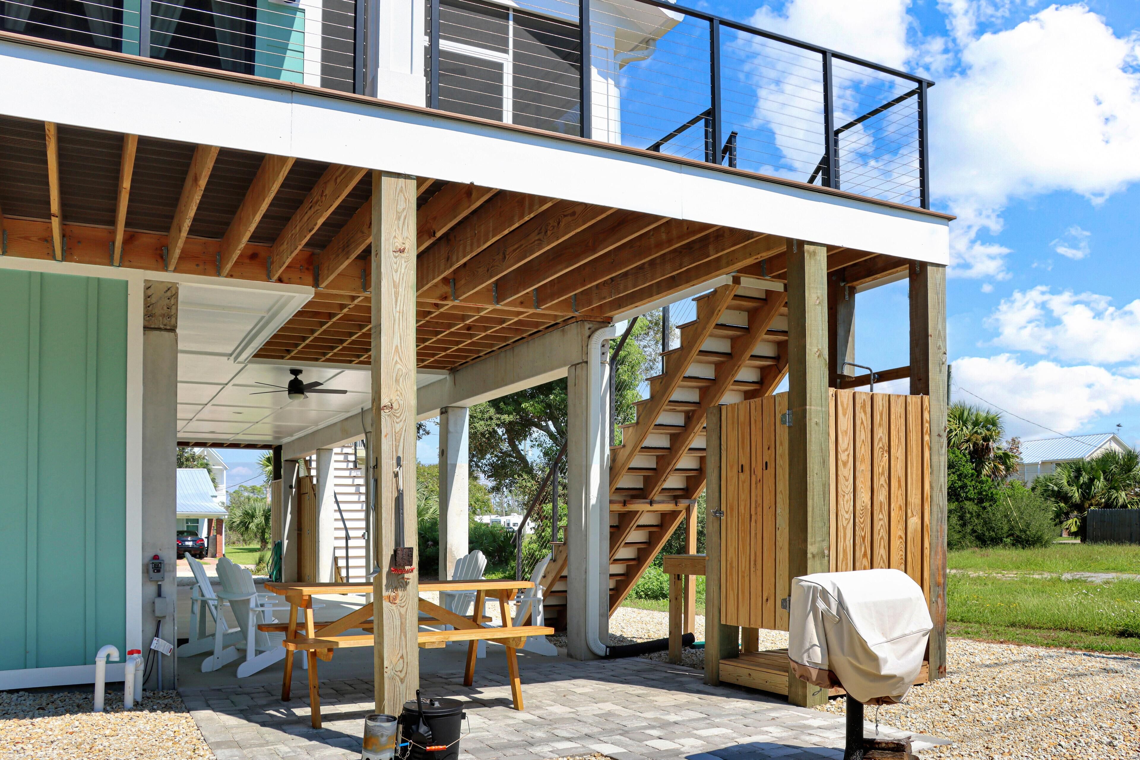 A modern house under construction with exposed wooden beams, a covered patio with outdoor furniture, and a staircase leading to an upper level.