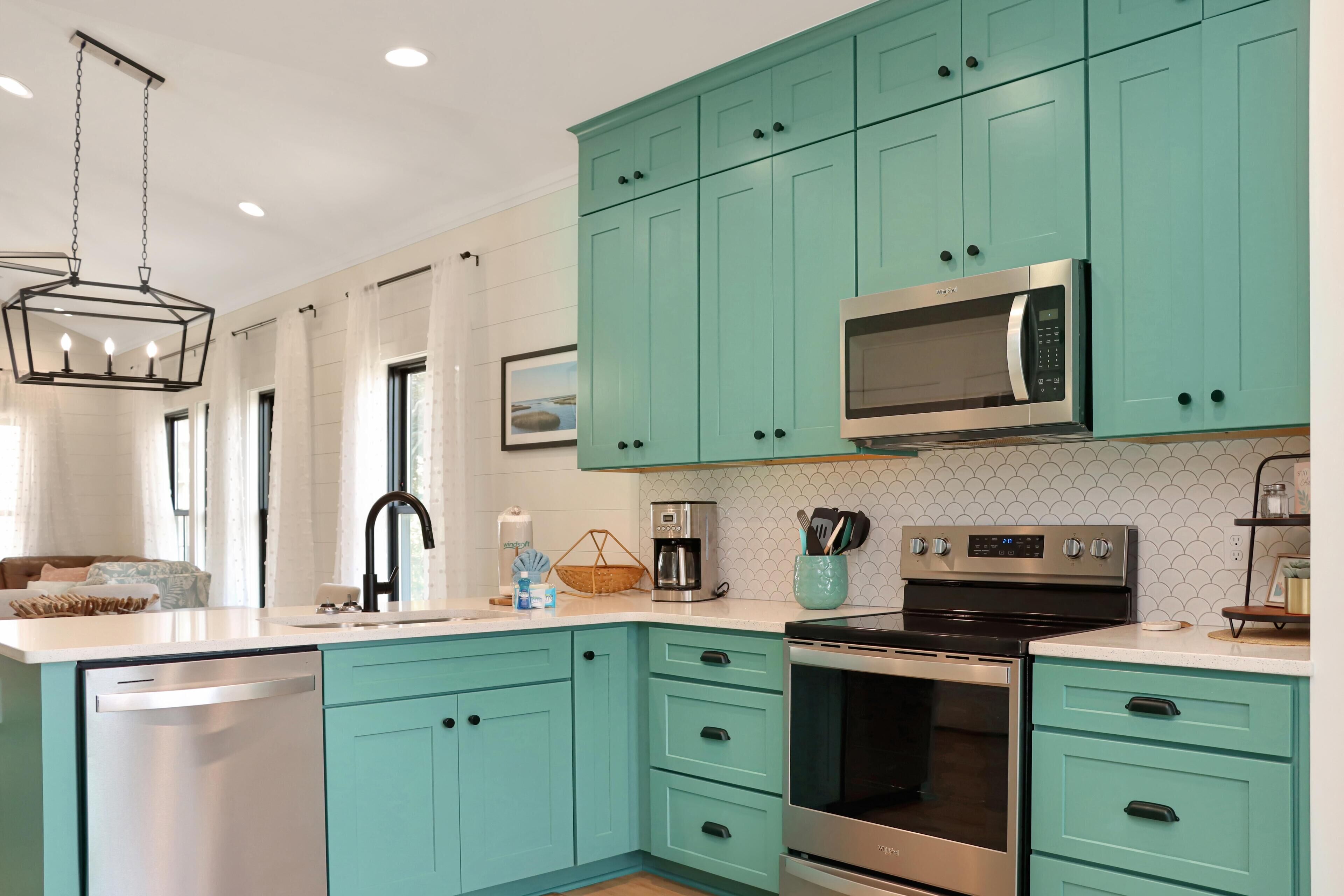 A modern kitchen with teal cabinets, stainless steel appliances, and a white tiled backsplash.