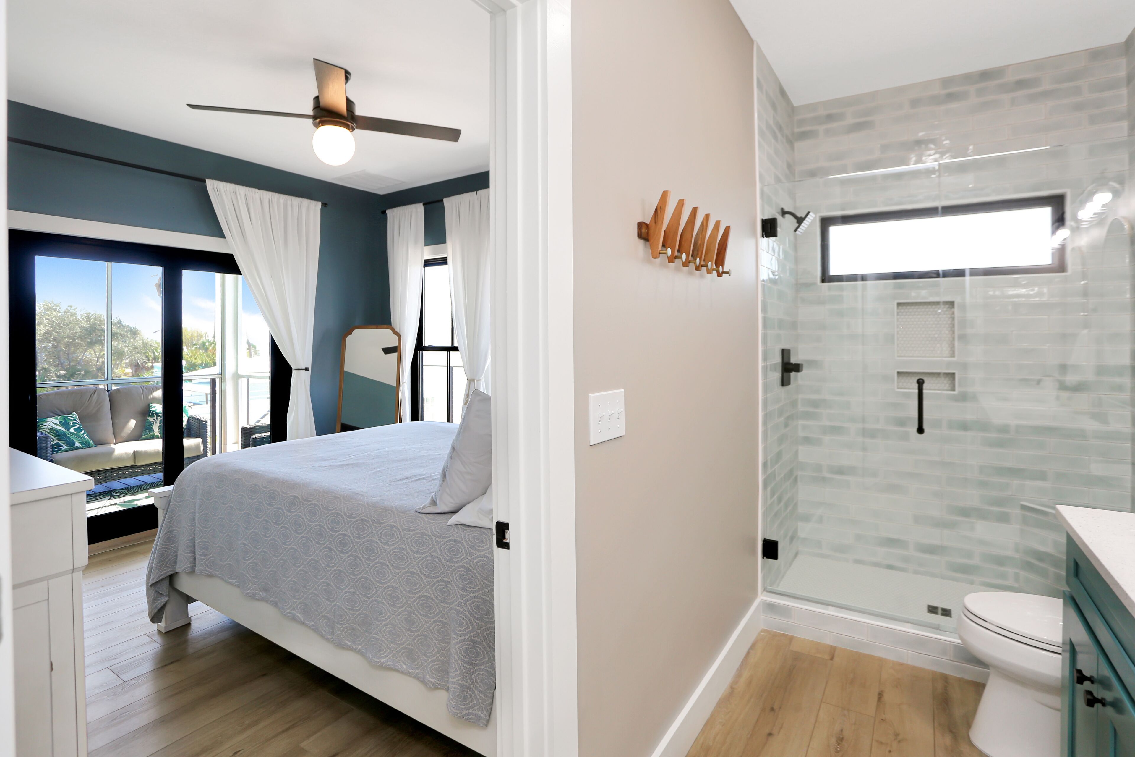 A bedroom with a bed, a ceiling fan, and a window with curtains. The bathroom features a glass shower enclosure, a toilet, and a sink.