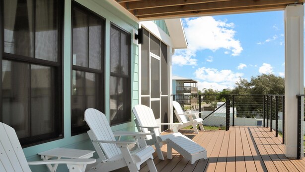 A covered outdoor deck with white Adirondack chairs and a table, overlooking a residential area. - Emerald Palms 3 (Port St. Joe)