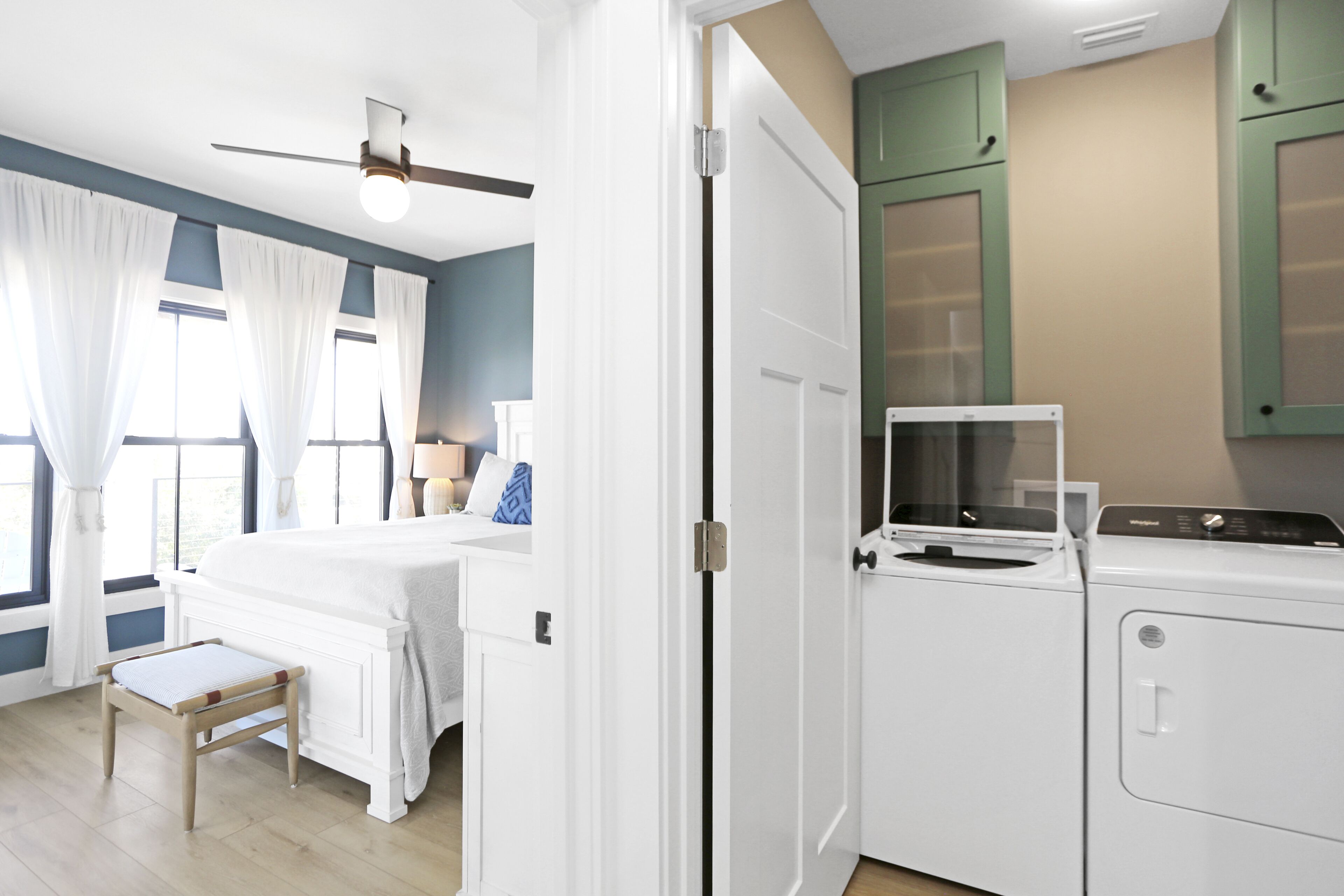 A bedroom with a bed, a nightstand, a window with curtains, a ceiling fan, and a washing machine.