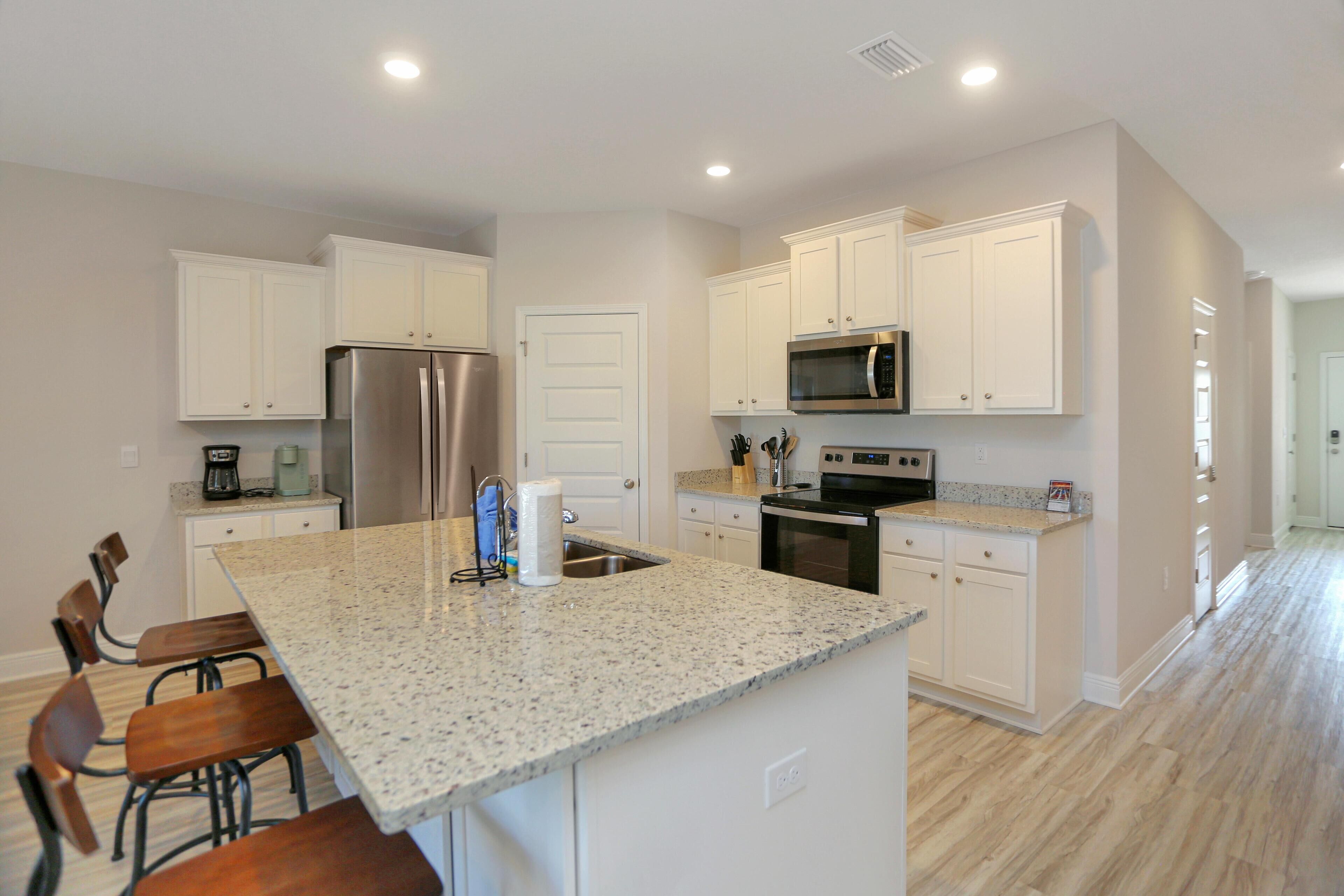 A kitchen with white cabinets, a granite countertop, a stainless steel refrigerator, and a microwave.