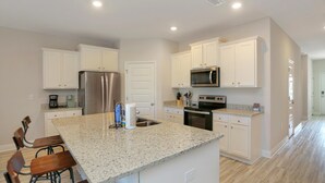 A kitchen with white cabinets, a granite countertop, a stainless steel refrigerator, and a microwave. - Paradise Isle (Port St. Joe)