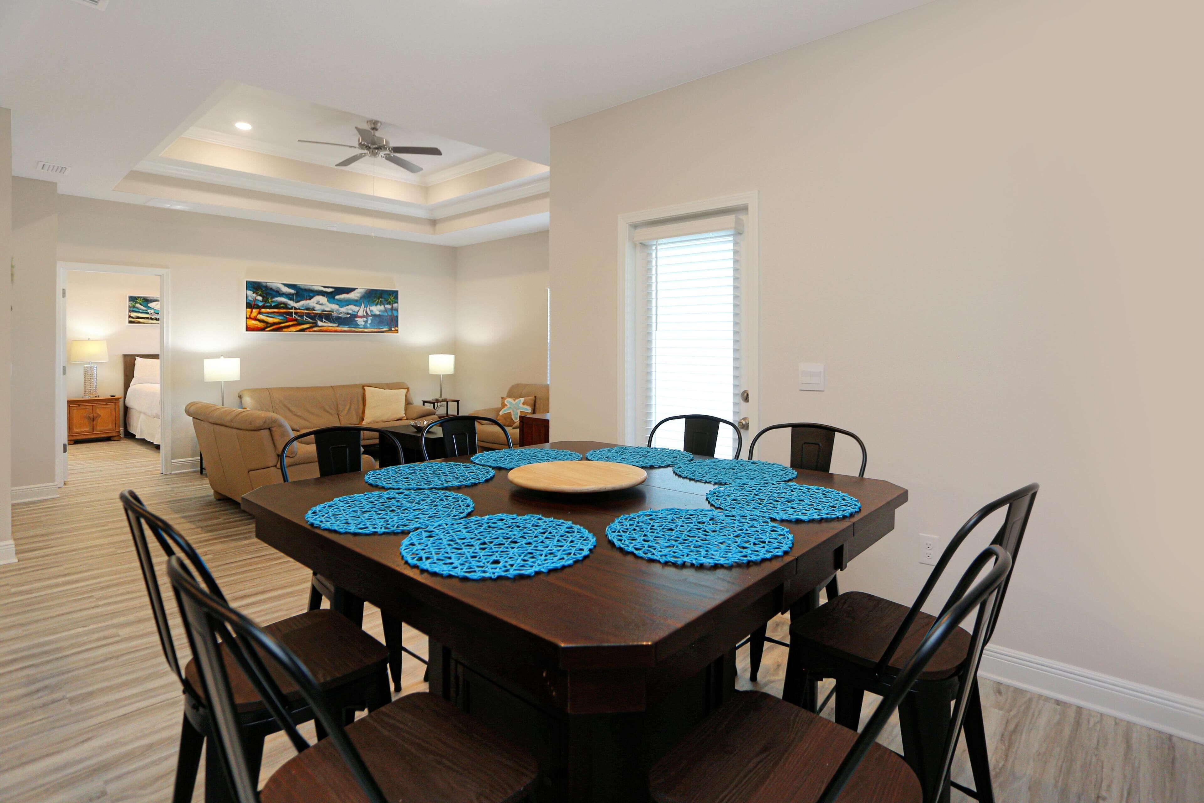 Un comedor con una mesa de madera oscura, seis sillas y manteles individuales azules.