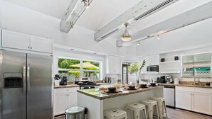 Uma cozinha moderna com armários brancos, eletrodomésticos de aço inoxidável e uma ilha central com banquetas.