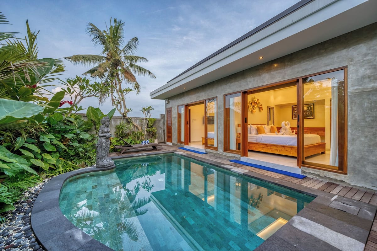Et moderne hus med swimmingpool, store vinduer og tropiske planter.
