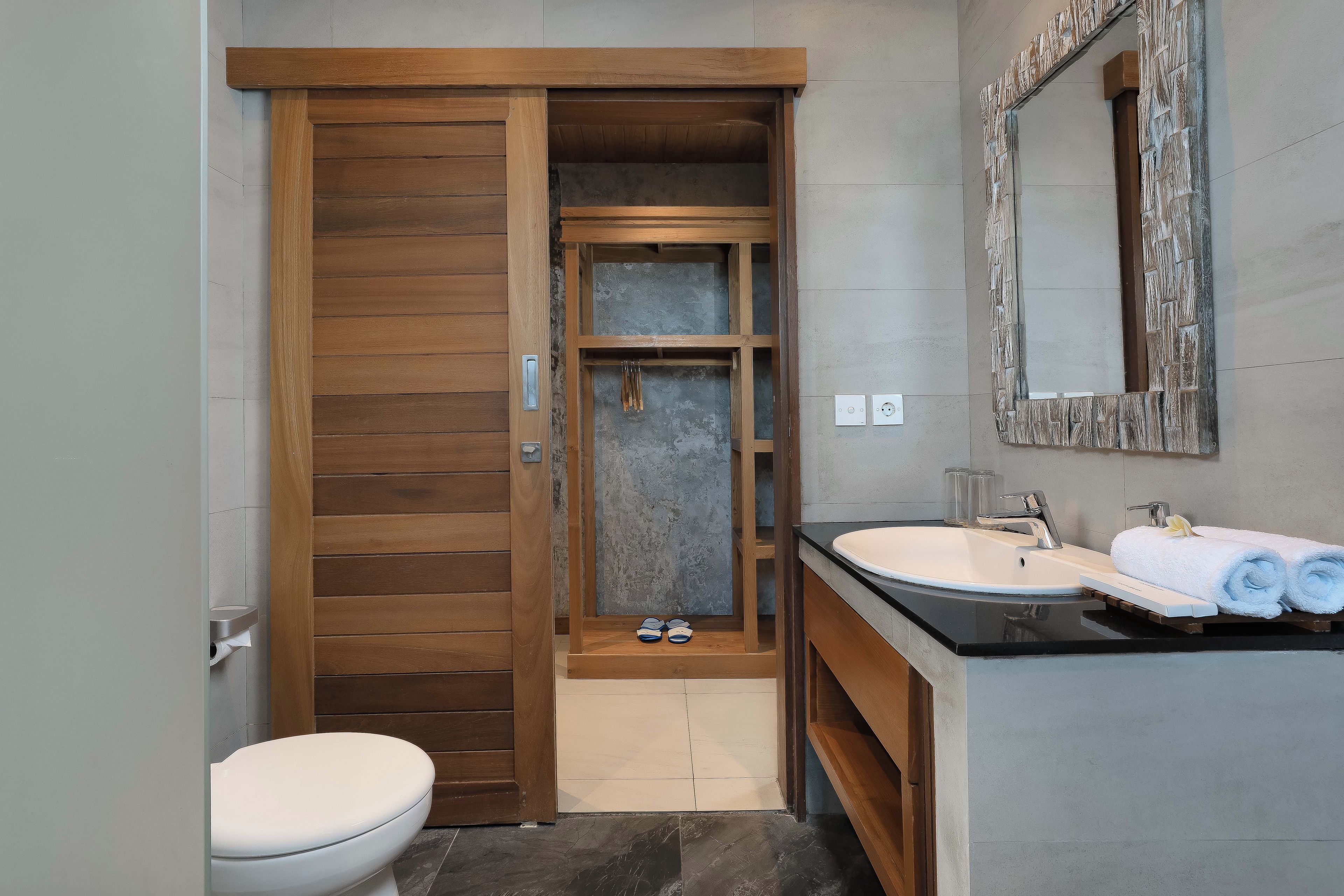 A bathroom with a wooden door, a toilet, a sink with a mirror, and a shower area.