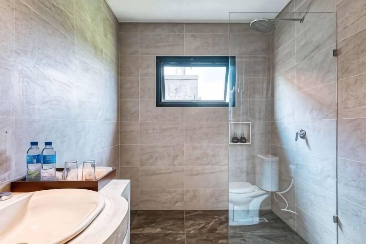 A bathroom with a bathtub, toilet, and shower area, featuring a window and tiled walls.