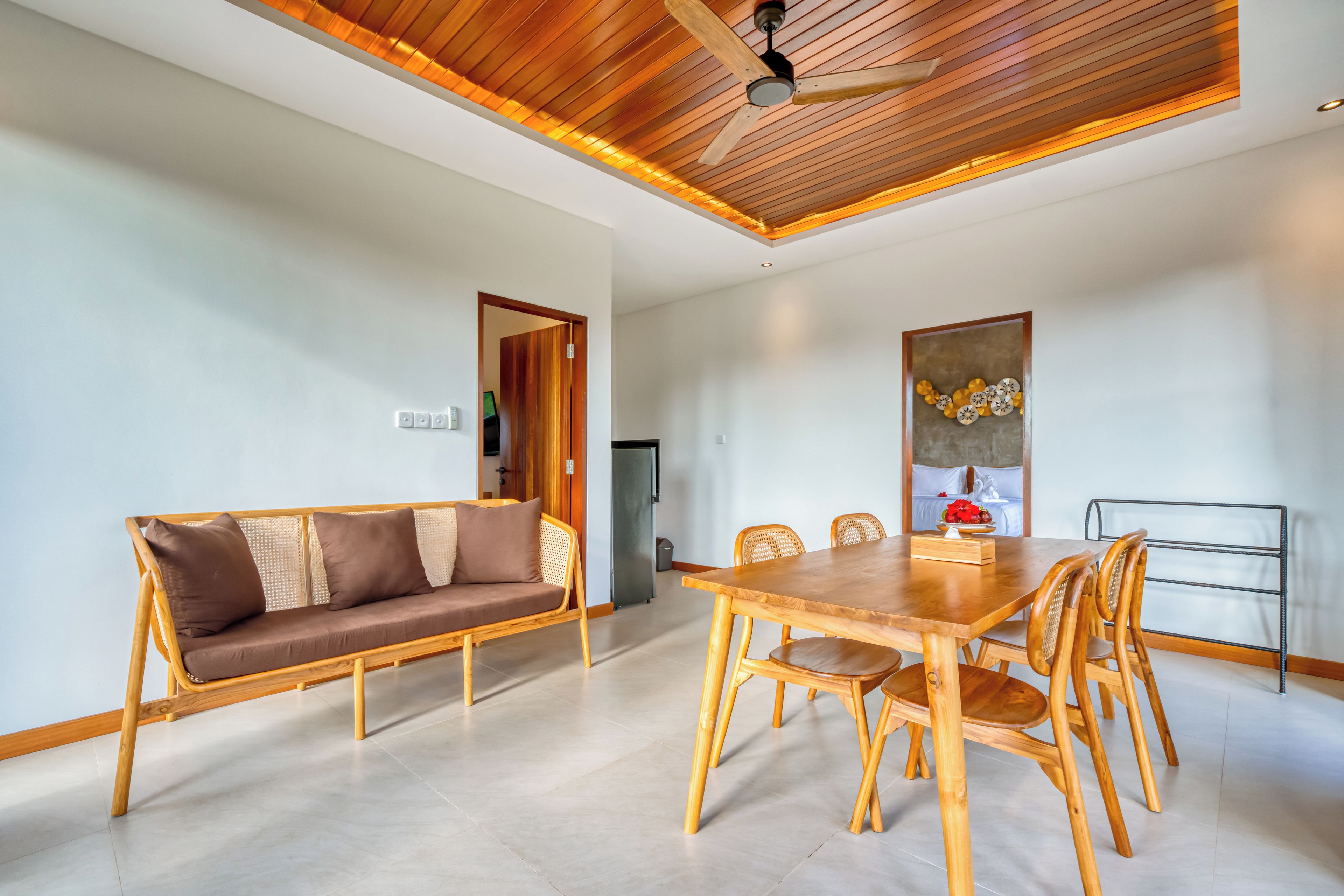A modern interior with a wooden ceiling, a dining area with a table and chairs, a sofa, and a wall-mounted artwork.