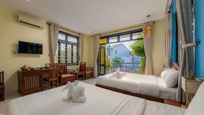 Quarto de hotel com duas camas, uma mesa com cadeira, televisão e varanda com vista para o exterior.