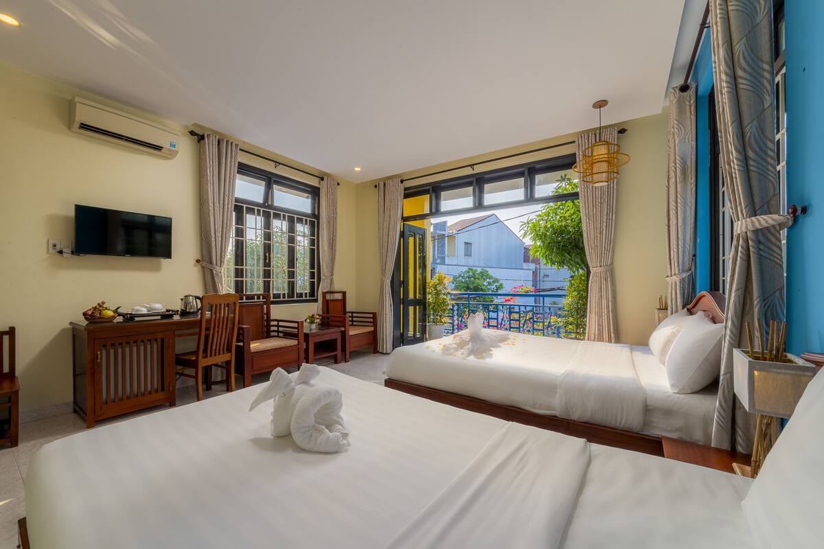 Ein Hotelzimmer mit zwei Betten, einem Schreibtisch mit Stuhl, einem Fernseher und einem Balkon mit Blick ins Freie.
