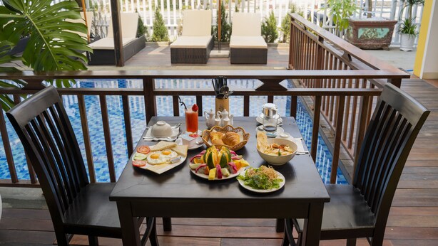 Mesa de jantar com itens de café da manhã, piscina e área de estar externa.