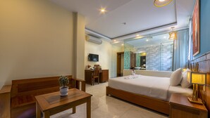 Quarto de hotel moderno com cama, móveis de madeira, televisão e banheiro com chuveiro de vidro.