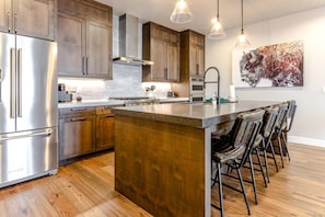 A modern kitchen with stainless steel appliances, wooden cabinets, and a central island with bar stools.