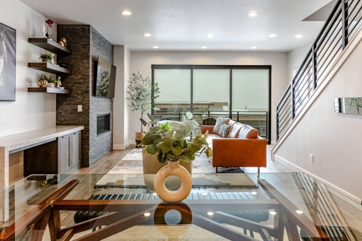 A modern living room with a glass coffee table, a fireplace, a sofa, and a staircase.
