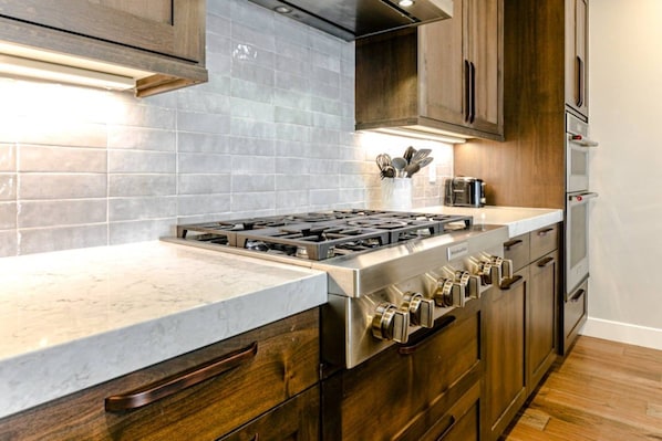 A kitchen with a stainless steel stove, wooden cabinets, and a marble countertop.